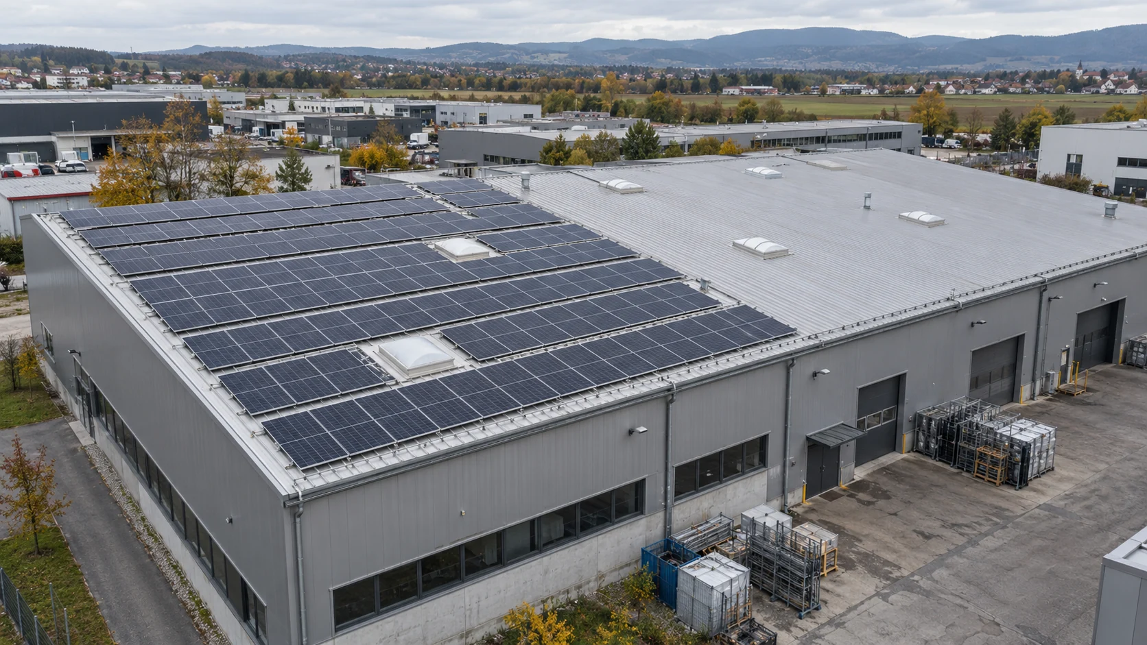 Industrial building with photovoltaic panels on part of its roof and an uncovered roof area.